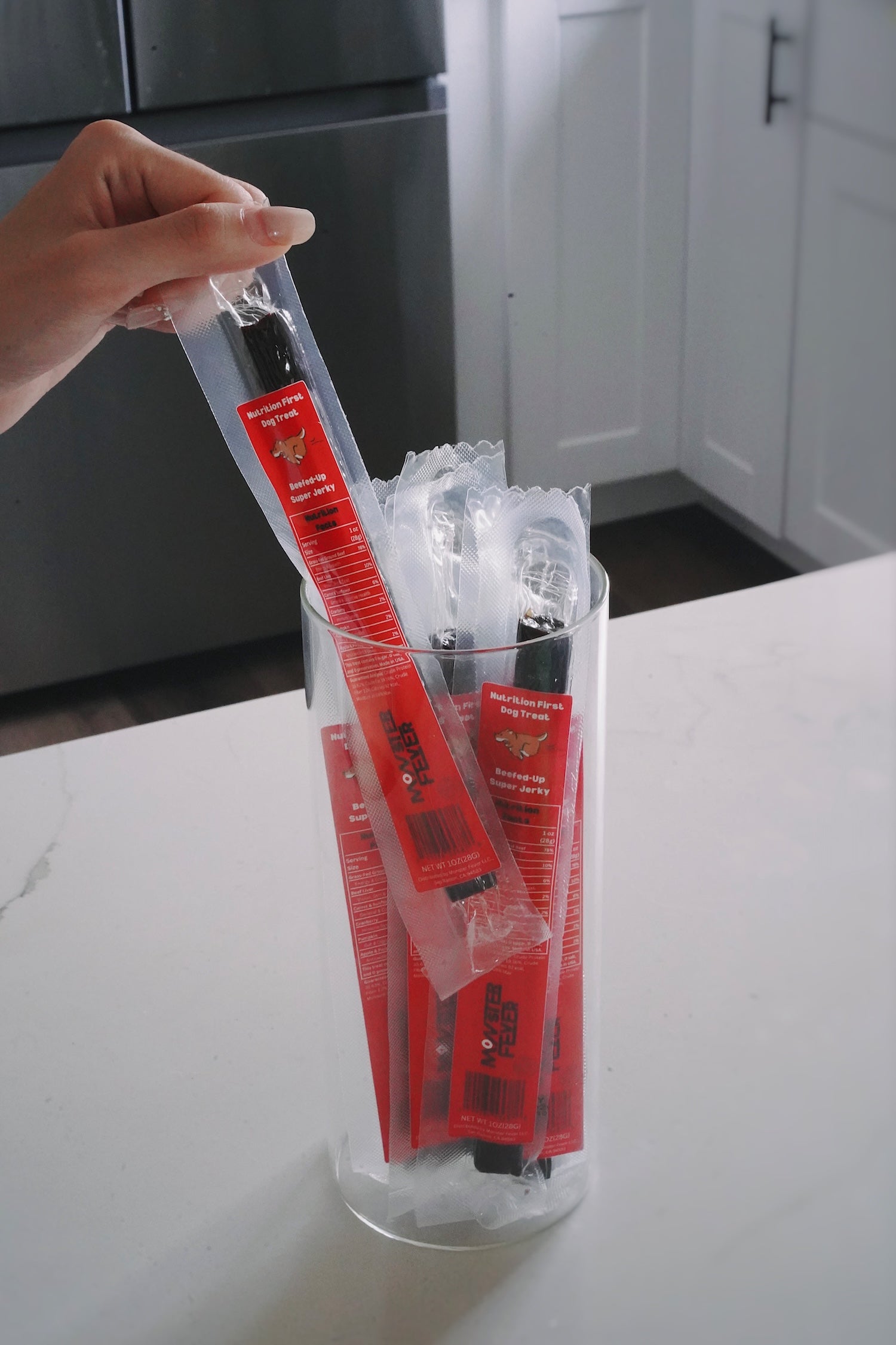 Individually wrapped jerky treat in a clear plastic packaging held by a hand on a kitchen counter.